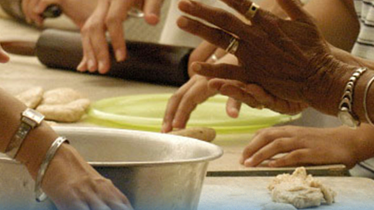 Many hands rolling and shaping dough together at a community kitchen table