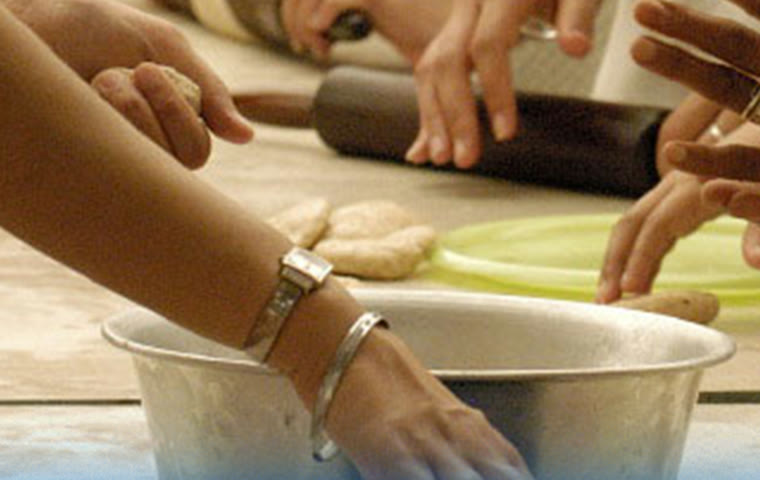 Many hands rolling dough together at a community kitchen table